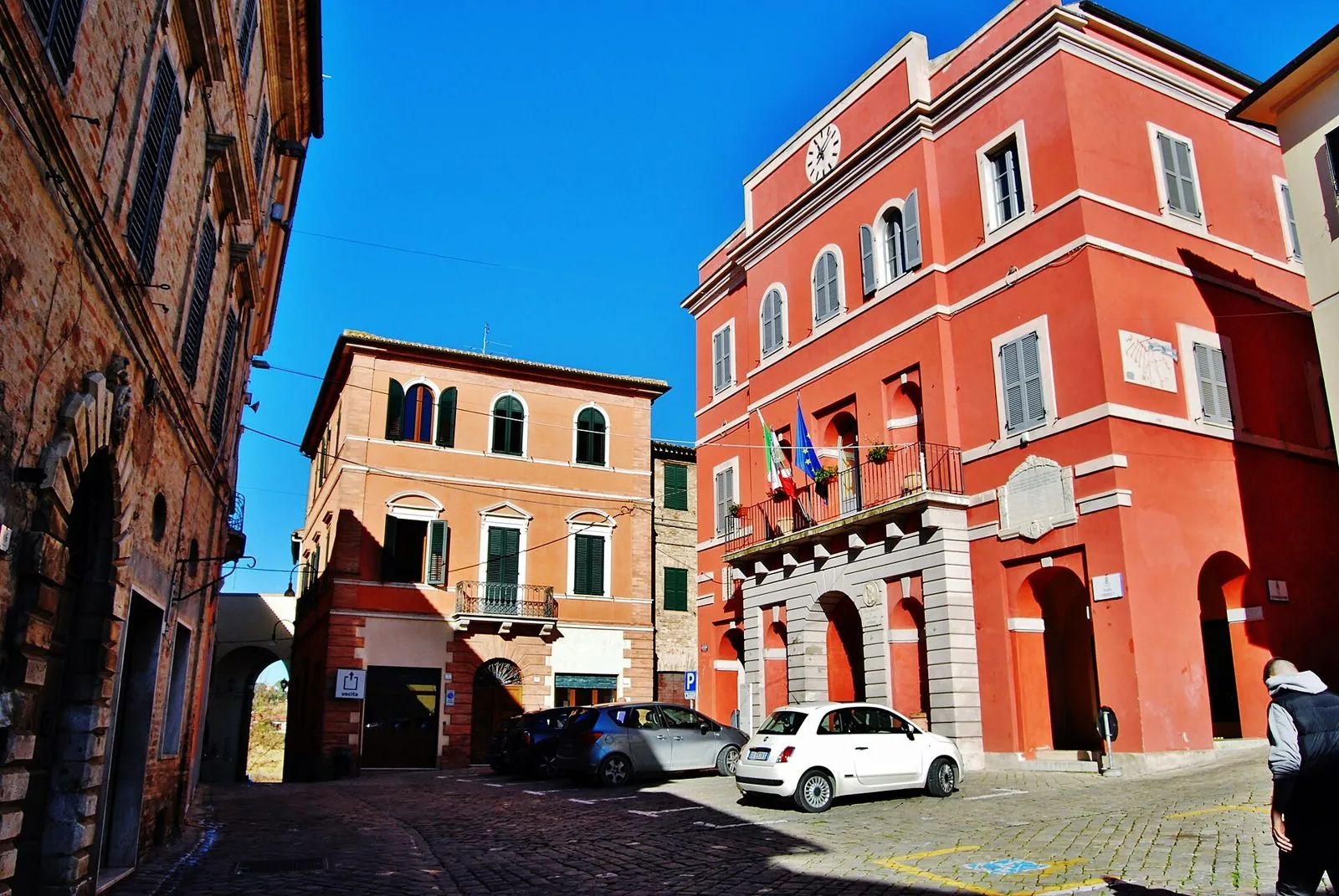 Piazza Umberto I ad Appignano con il Palazzo Comunale rosso e gli edifici storici in mattoni sotto il cielo azzurro